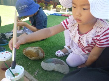 Two children painting stones outside