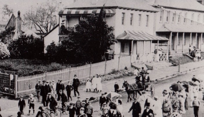 A parade passing by colonial buildings in the 1870s
