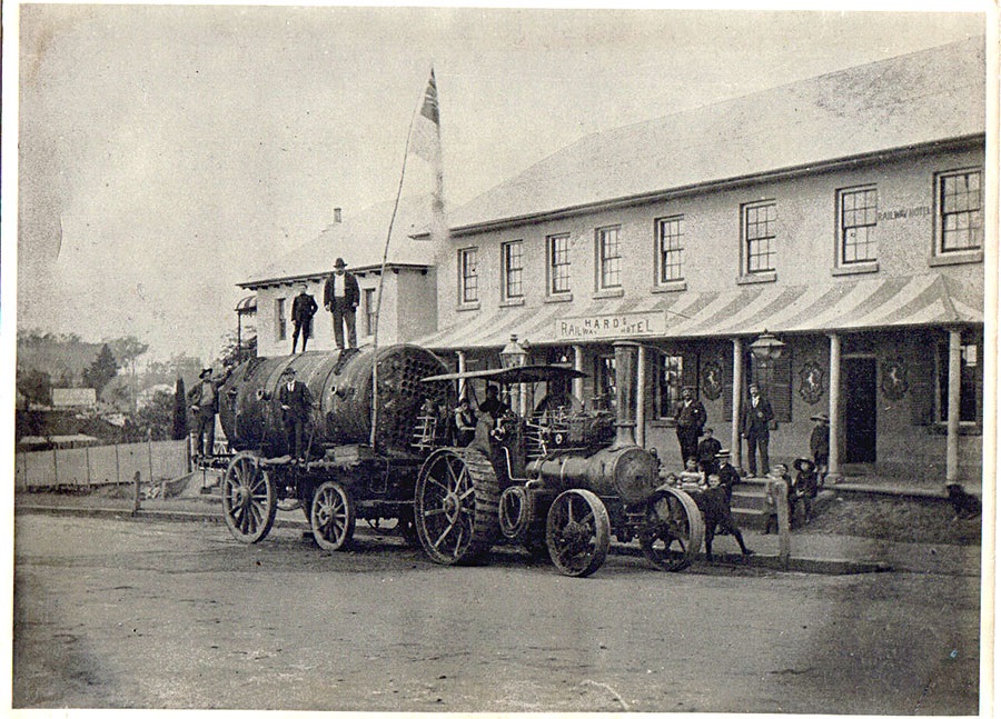 A steam engine on an old wagon passing an old hotel