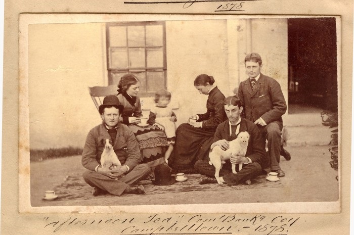 A sepia photograph of a small family group enjoying afternoon tea 