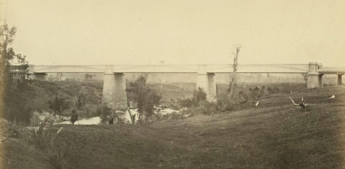 black and white photo of the Menangle bridge with a train approaching from the left 