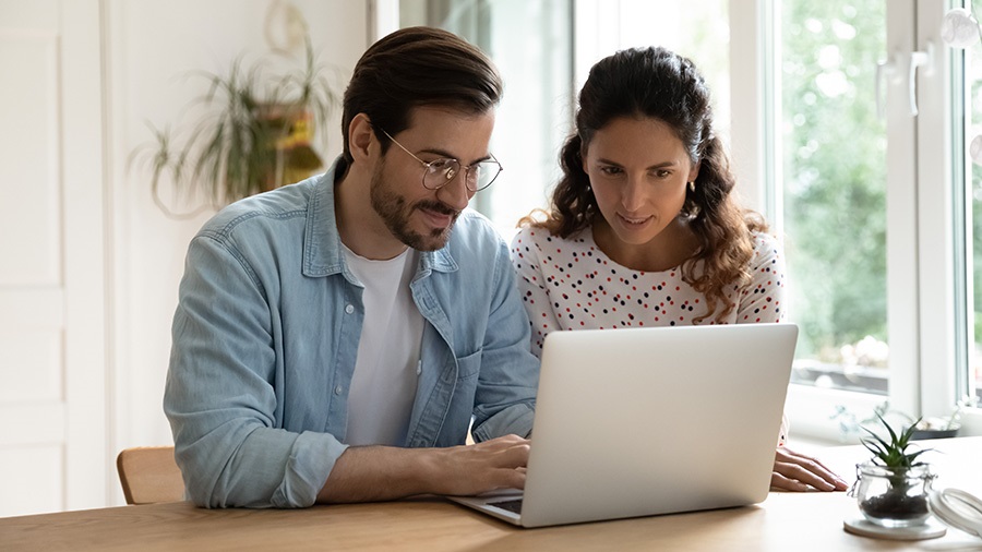 A man and a woman sitting at a table looking at a laptop computer