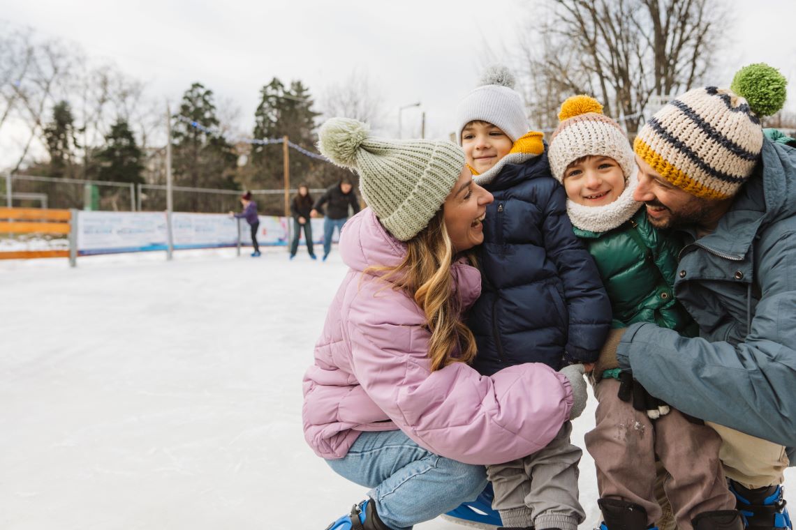 Young family hugging on an ice skating rink, dressed in winter clothes.