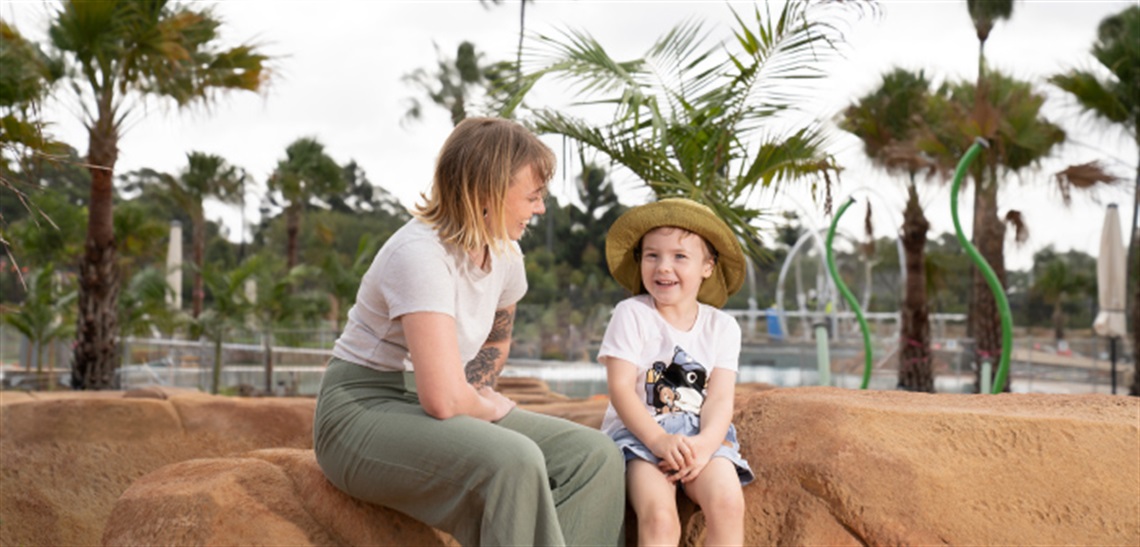 Lady sitting with young boy on rocks in water splash play area at Billabong Parklands
