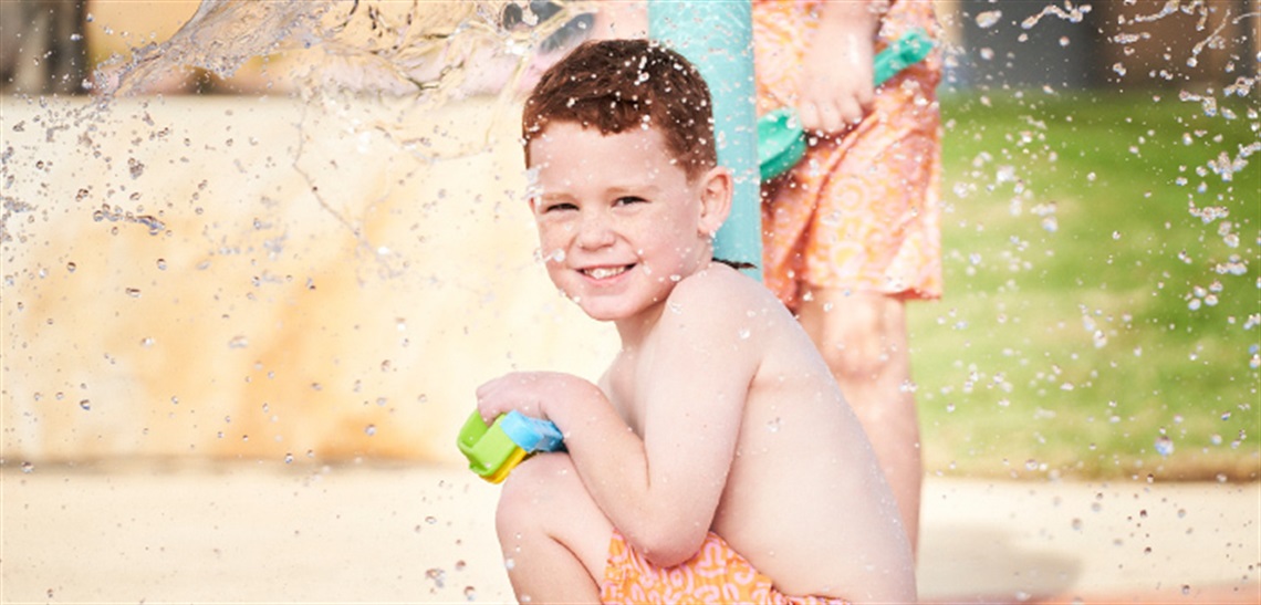 A boy smiling at the camera while playing in the Billabong Parklands Splash Play area
