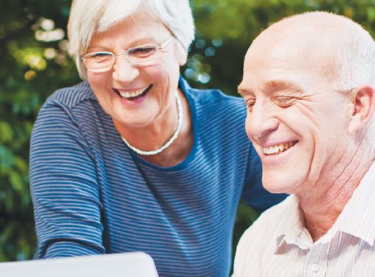 Two seniors smiling with confidence whilst looking at a computer